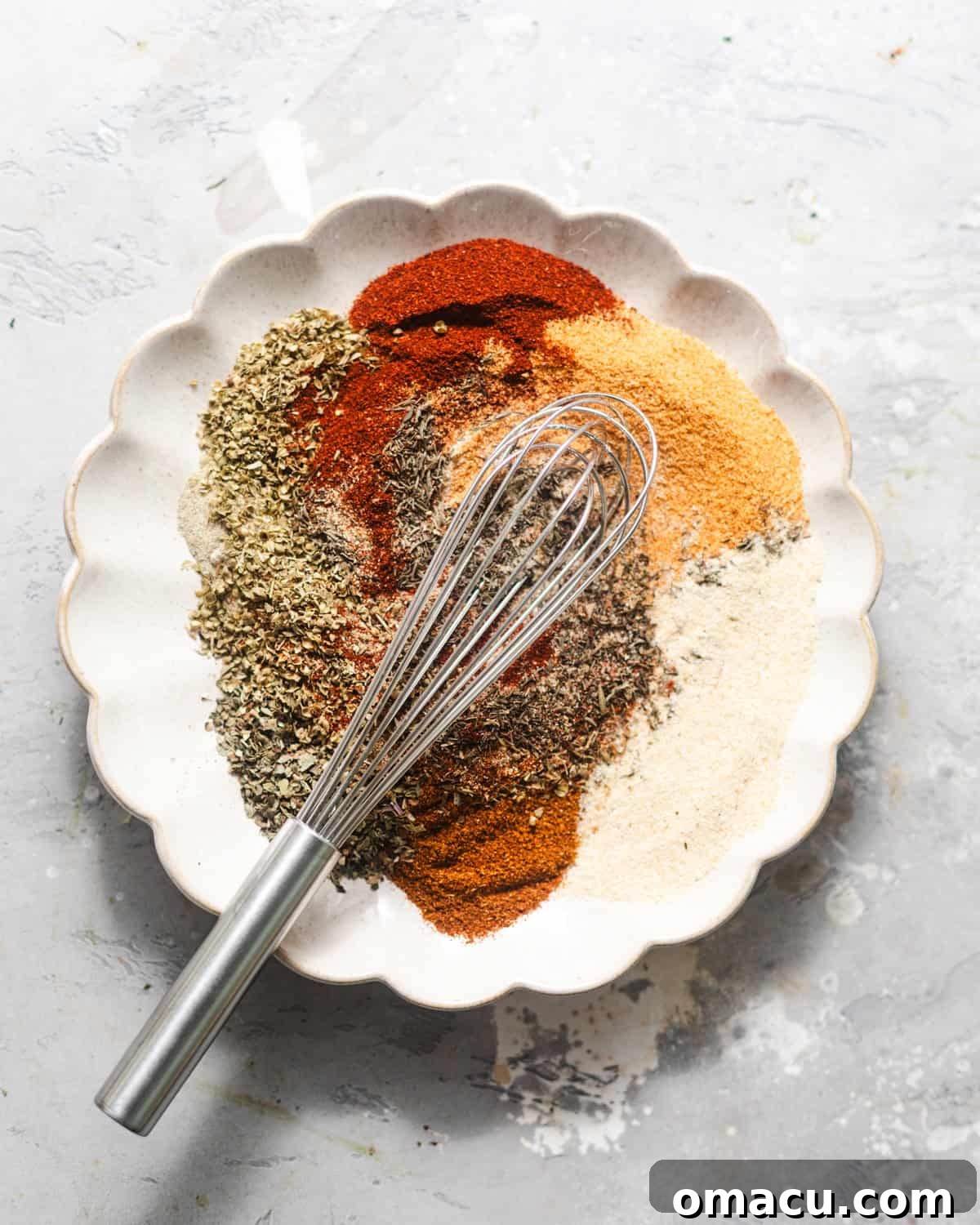 Various spices on a plate being mixed together with a small whisk.