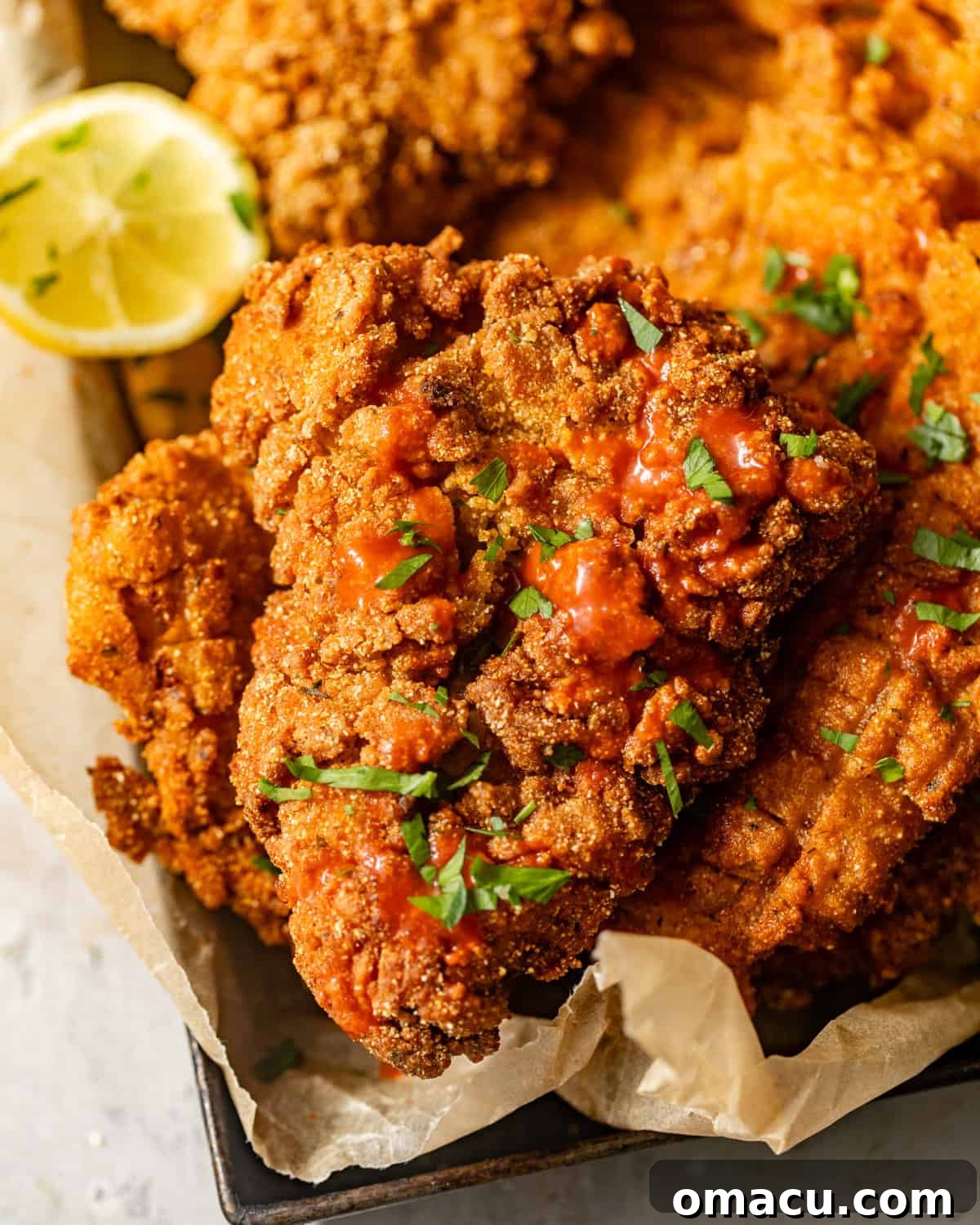 Close-up of freshly fried catfish in a serving basket, garnished with vibrant fresh parsley and bright lemon wedges, ready to be enjoyed.