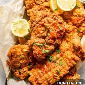 Crispy fried catfish in a basket lined with parchment paper, garnished with lemon slices.