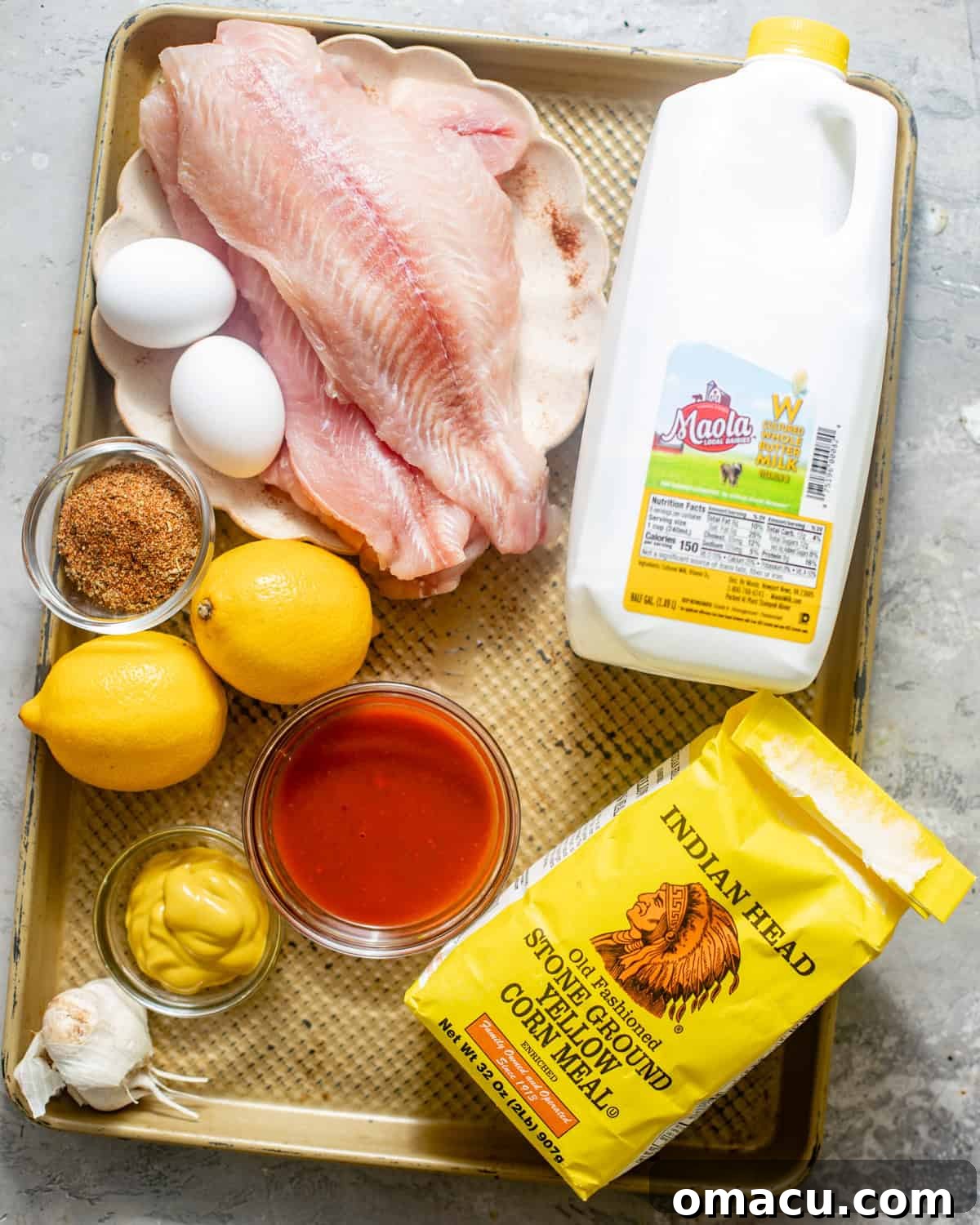 A vibrant flat lay of all essential ingredients to make Southern fried catfish, including fresh catfish fillets, buttermilk, lemon, hot sauce, yellow cornmeal, all-purpose flour, and a variety of aromatic seasonings.