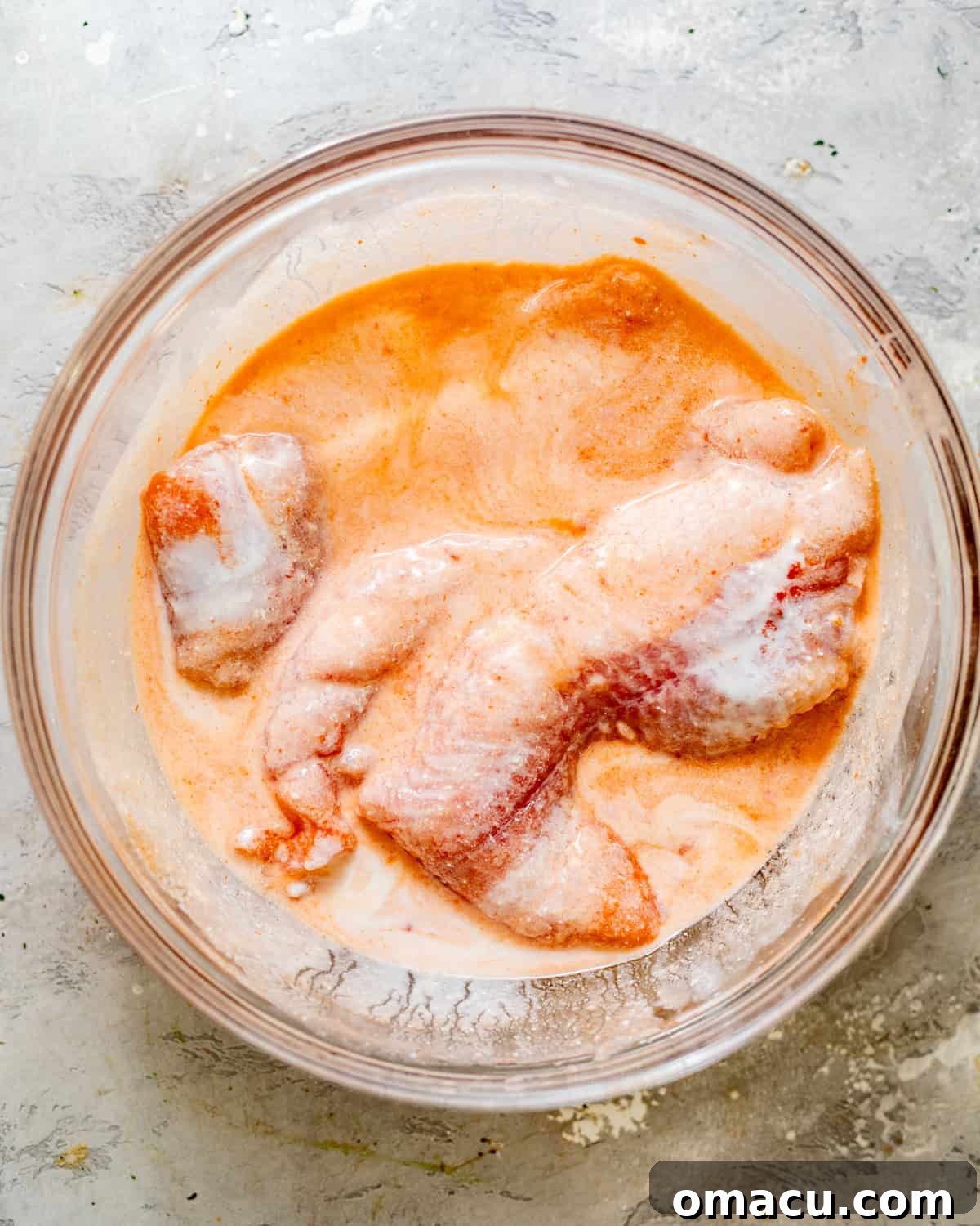 Fresh catfish fillets submerged in a milky buttermilk brine within a clear mixing bowl, ready for marination.