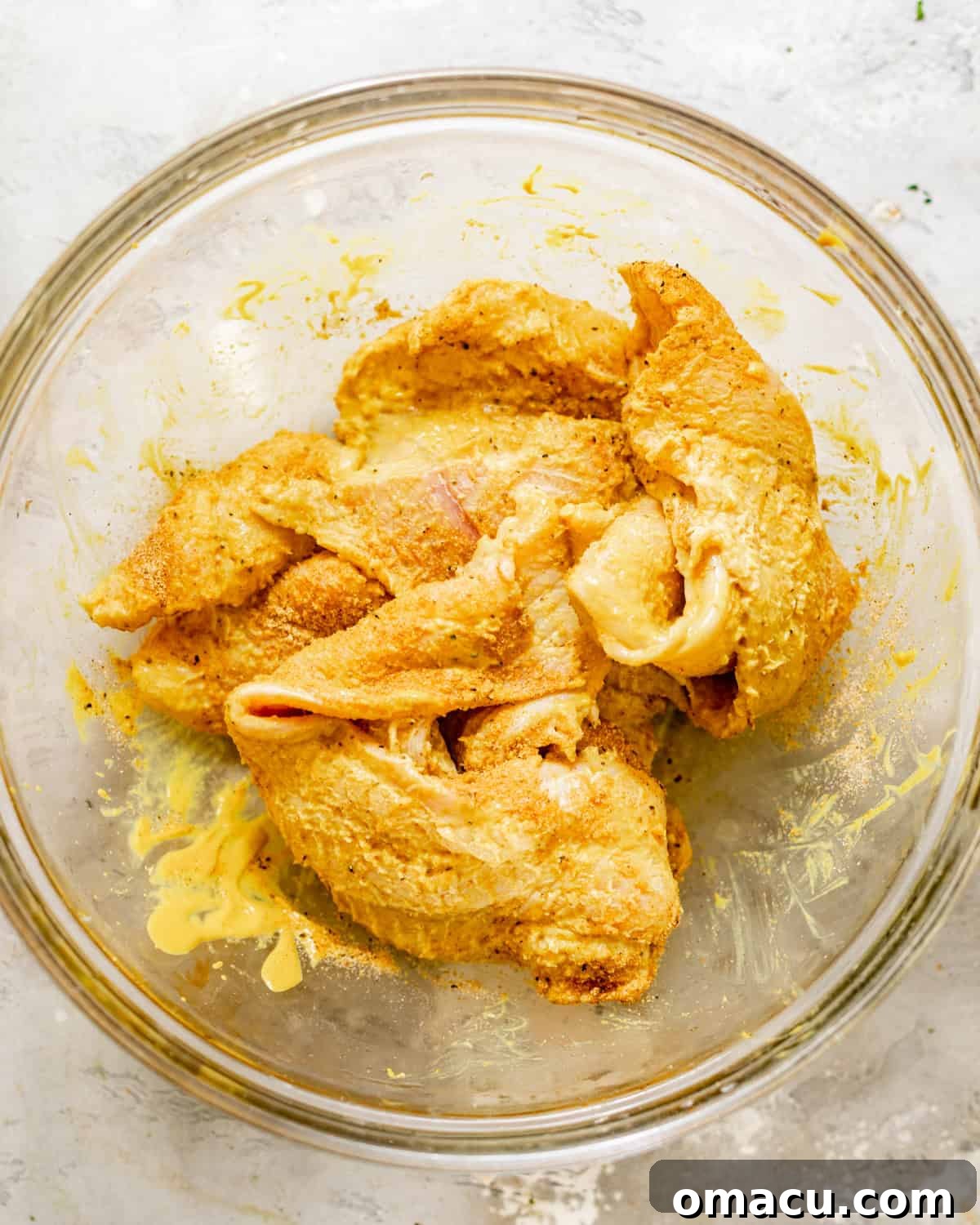 Cut catfish pieces coated in bright yellow mustard and a robust blend of dry spices, tossed in a mixing bowl.