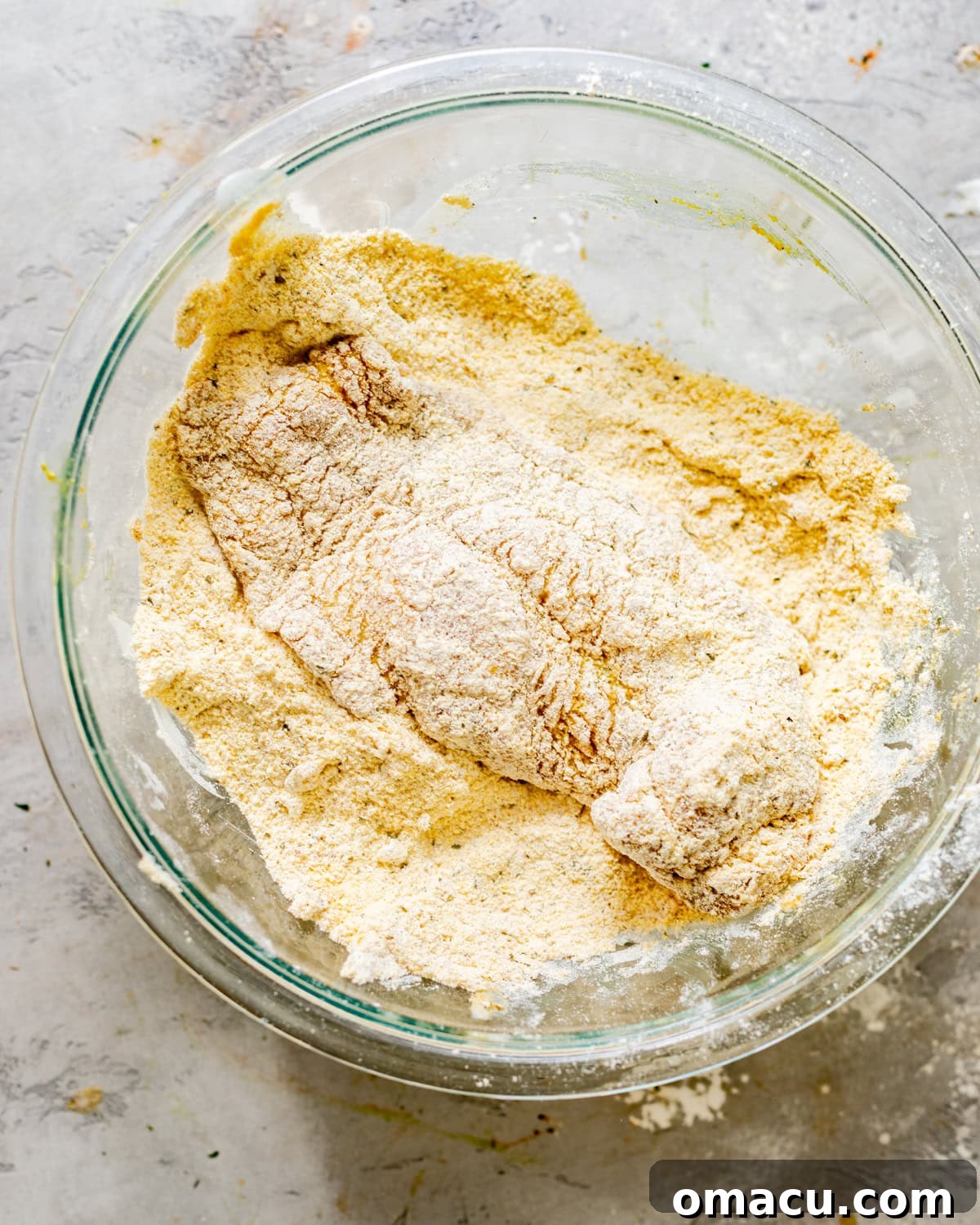 Catfish fillet being thoroughly coated in the seasoned cornmeal dredge in a bowl, showing the texture.