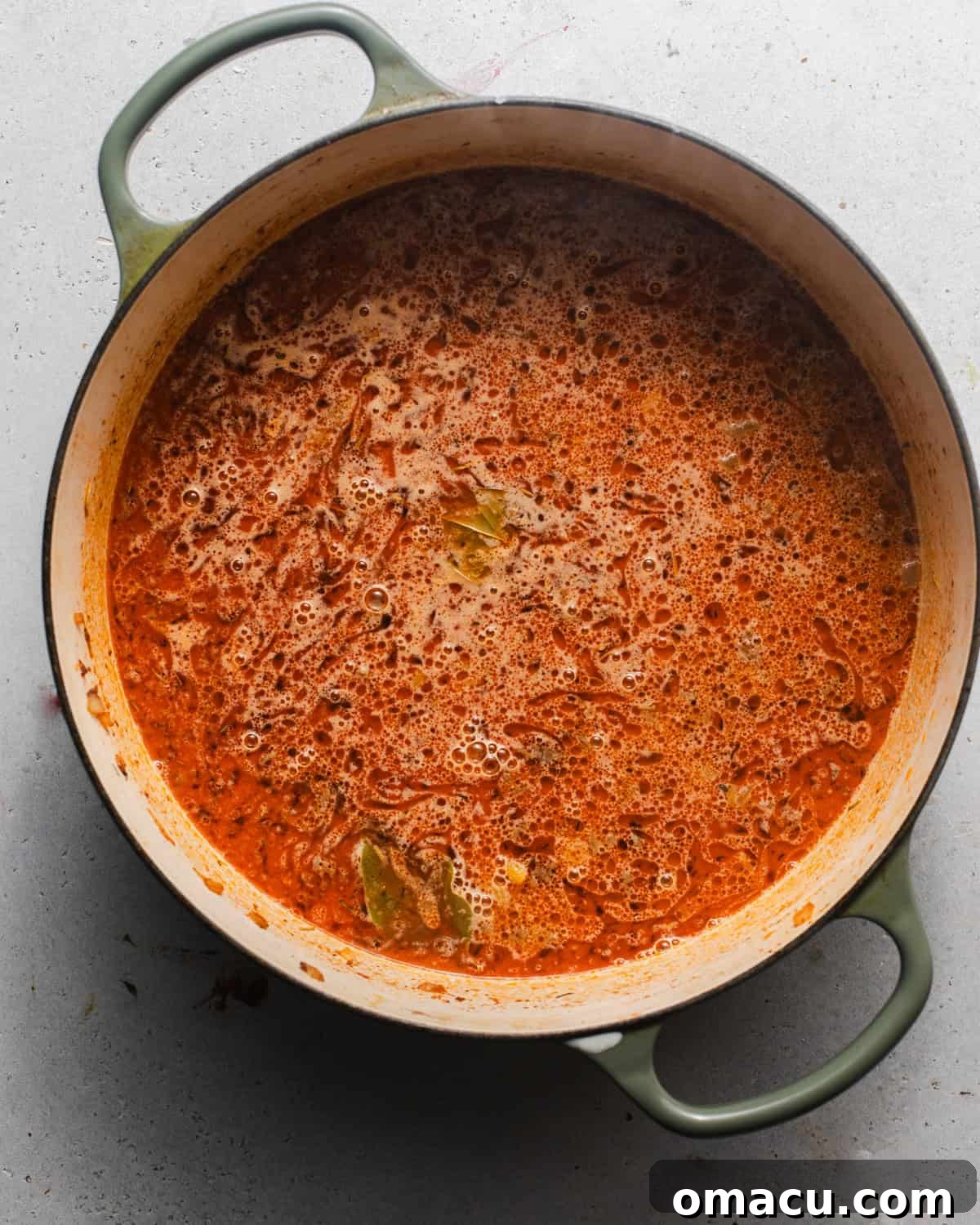 Beef broth being poured into the pot with browned ground beef and seasonings.