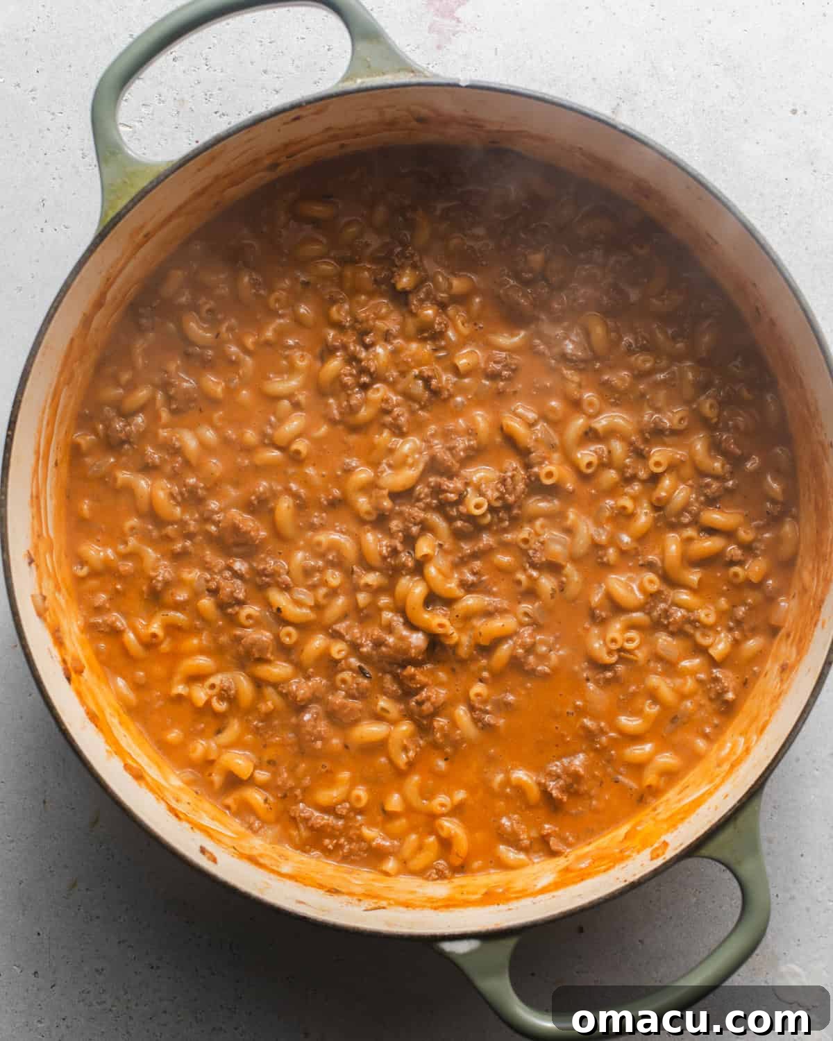 Elbow macaroni and heavy cream added to the pot with the beef and broth, simmering.