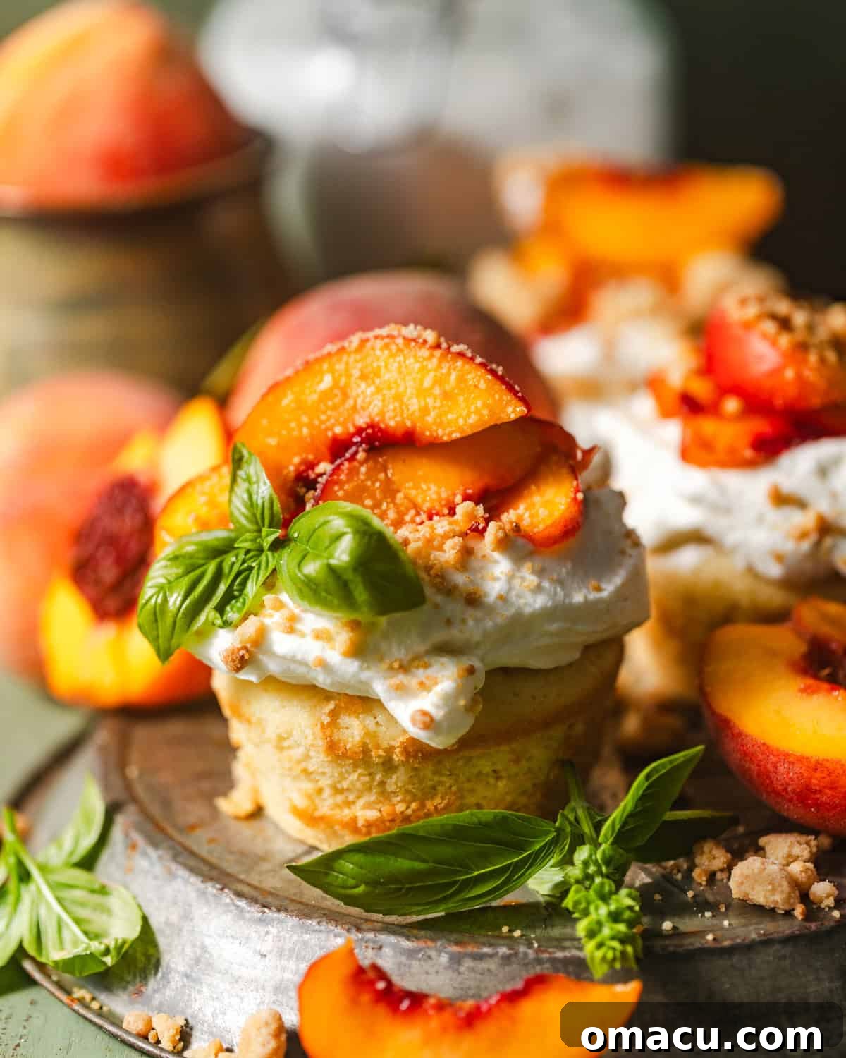 Four peach shortcakes arranged on a ceramic pie plate, garnished with vibrant macerated peaches, a generous dollop of whipped cream, and fresh basil leaves.