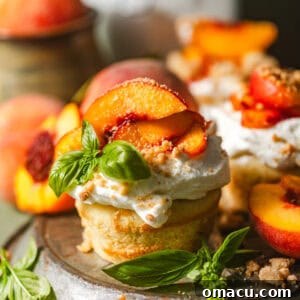 A close-up of beautifully assembled peach shortcakes on a pie plate, adorned with macerated peaches, whipped cream, and fresh basil for garnish.