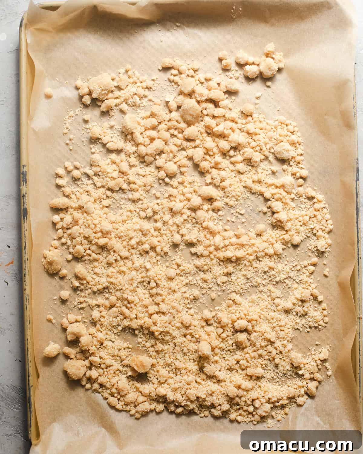 A baking sheet lined with parchment paper, topped with a golden-brown cinnamon crumble cooling down.