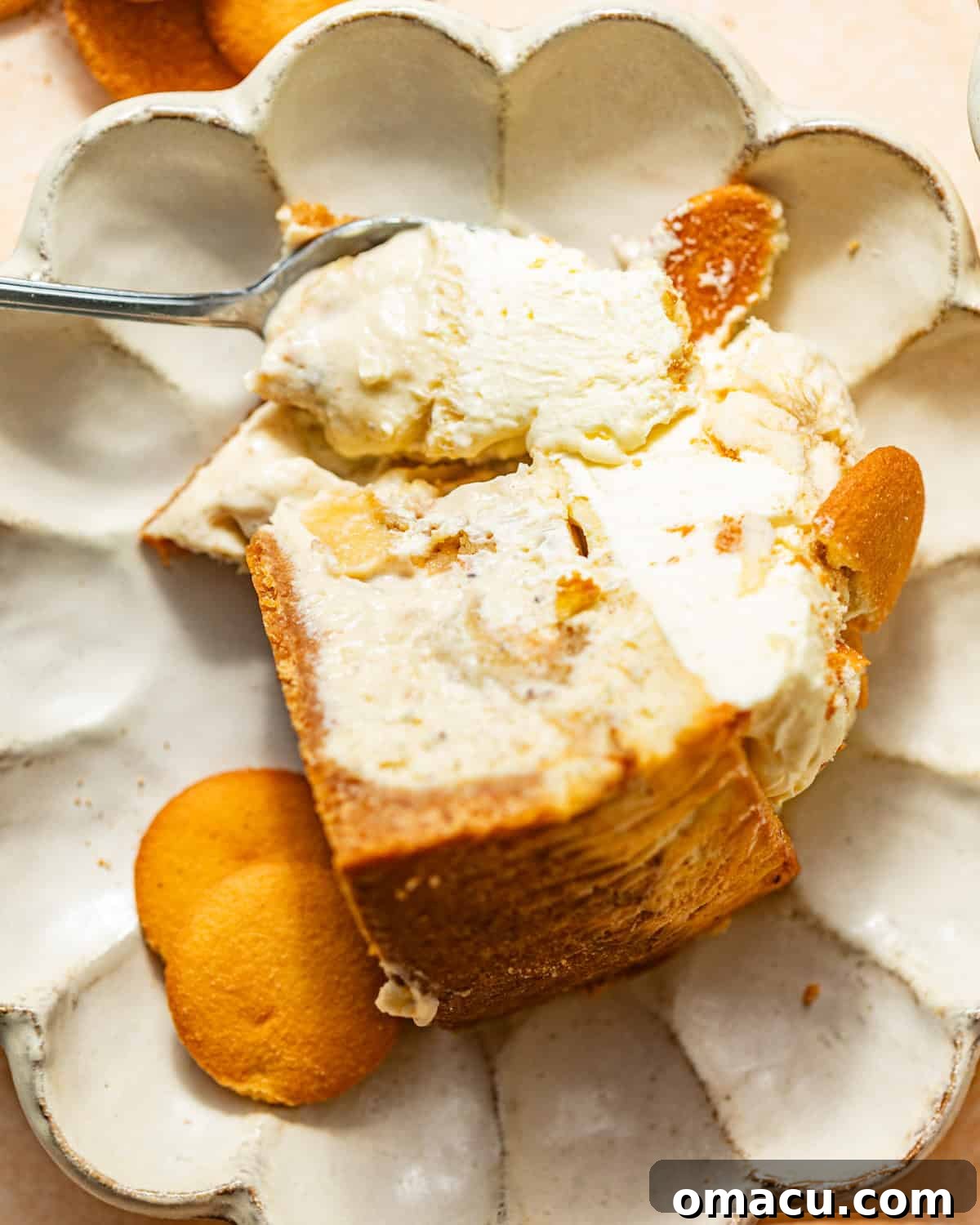 A perfectly sliced banana pudding cheesecake on a white plate, accompanied by a spoon and whole Nilla wafers, showing its creamy layers.