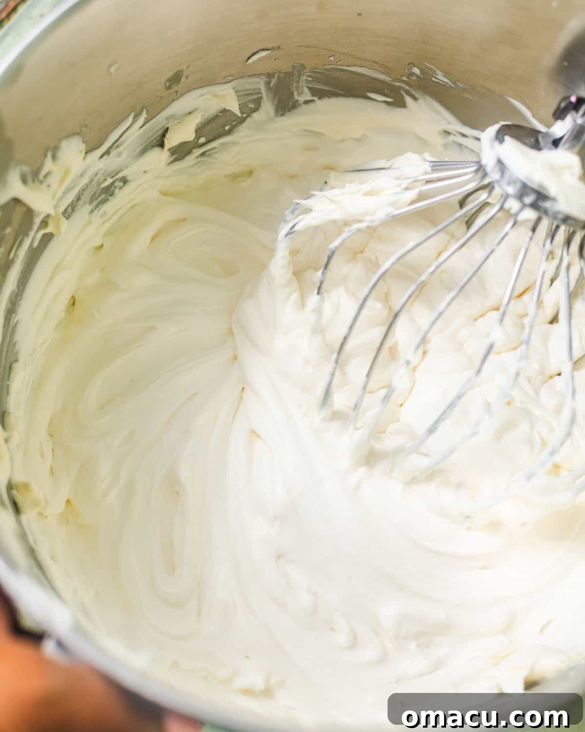 A large mixing bowl containing a creamy mixture of whipped cream, sweetened condensed milk, and mascarpone, perfectly whisked together to soft peaks.