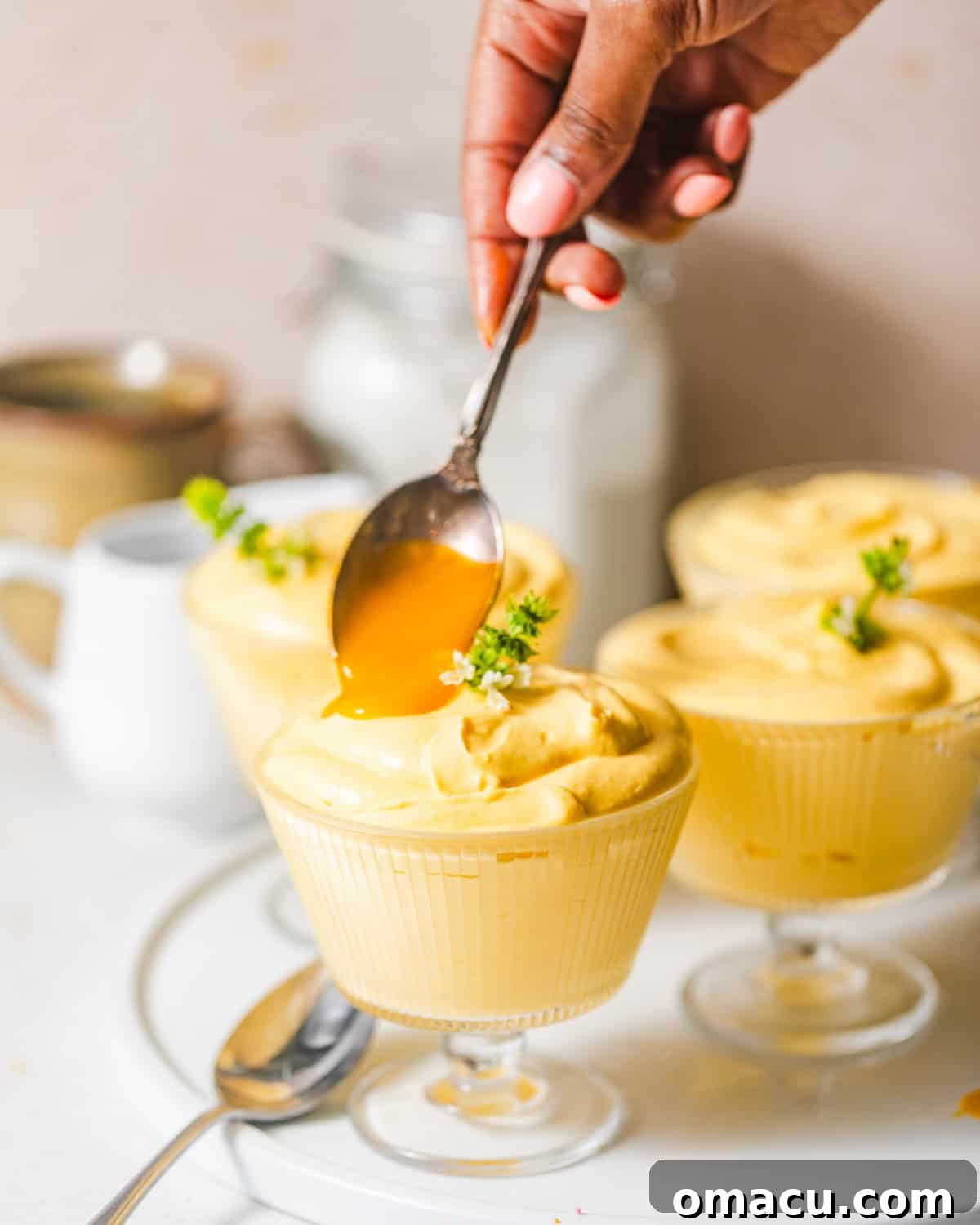 A spoon delicately adding more mango puree as a topping onto the set mango mousse cups, ready for final garnishes.