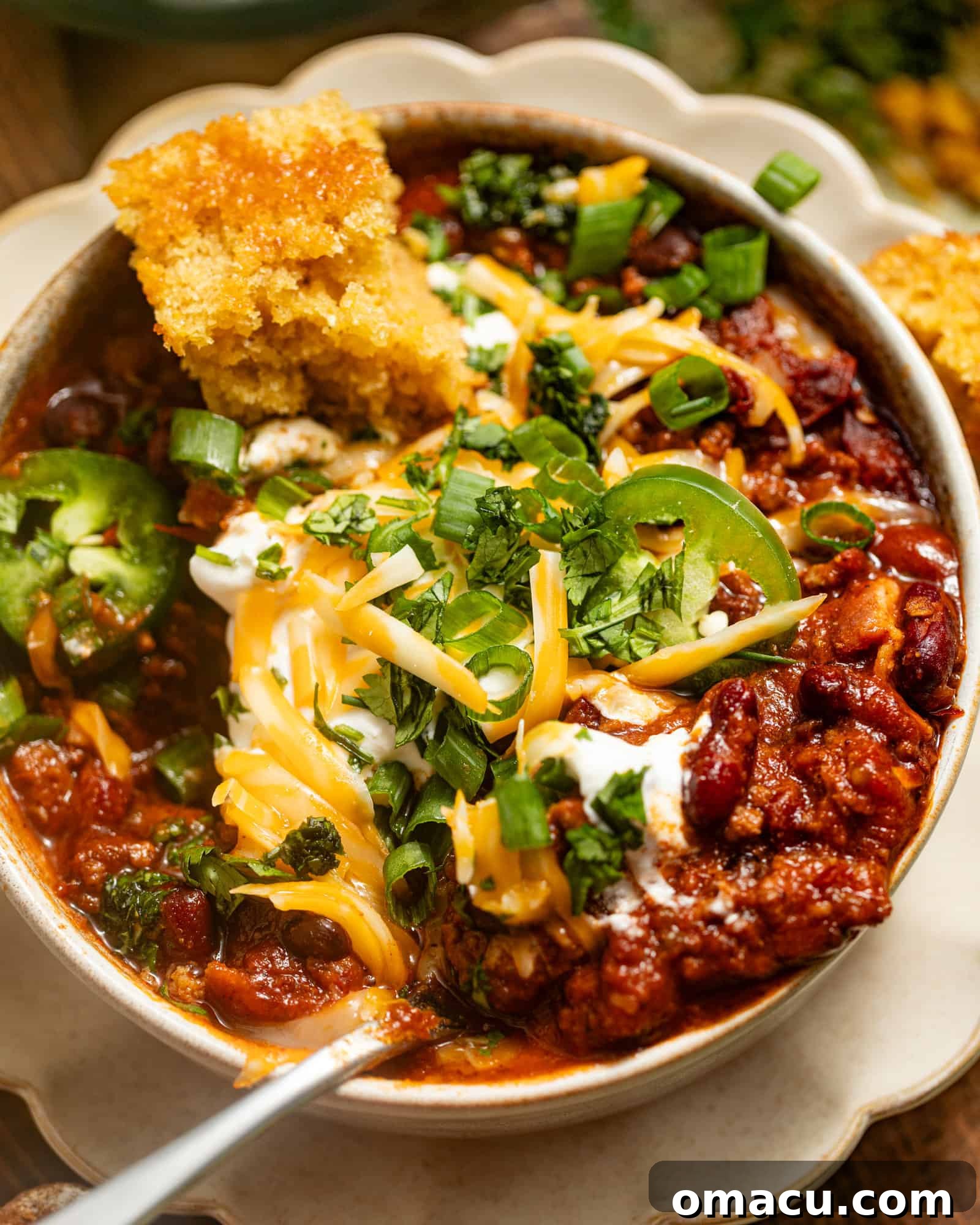 Up close photo of a bowl of rich, hearty Dutch oven chili, topped with vibrant fresh cilantro and melted cheddar cheese, with a spoon resting in it.