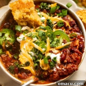 Up close photo of chili in a bowl with a spoon and topped with cilantro and cheese.