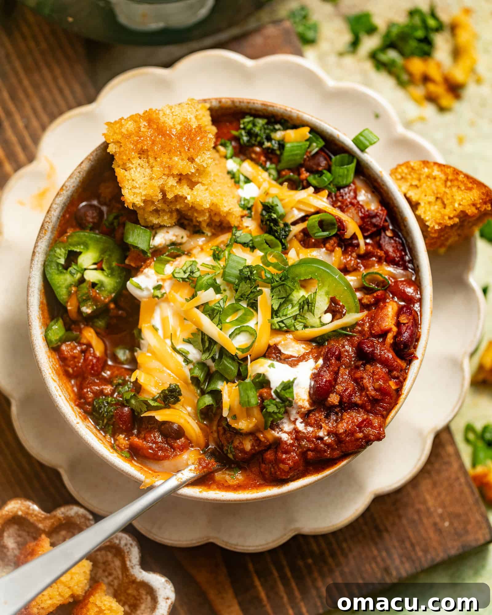 A vibrant bowl of homemade chili garnished with fresh jalapeños, cooling sour cream, crunchy tortilla chips, and melted cheese, set on a rustic plate.
