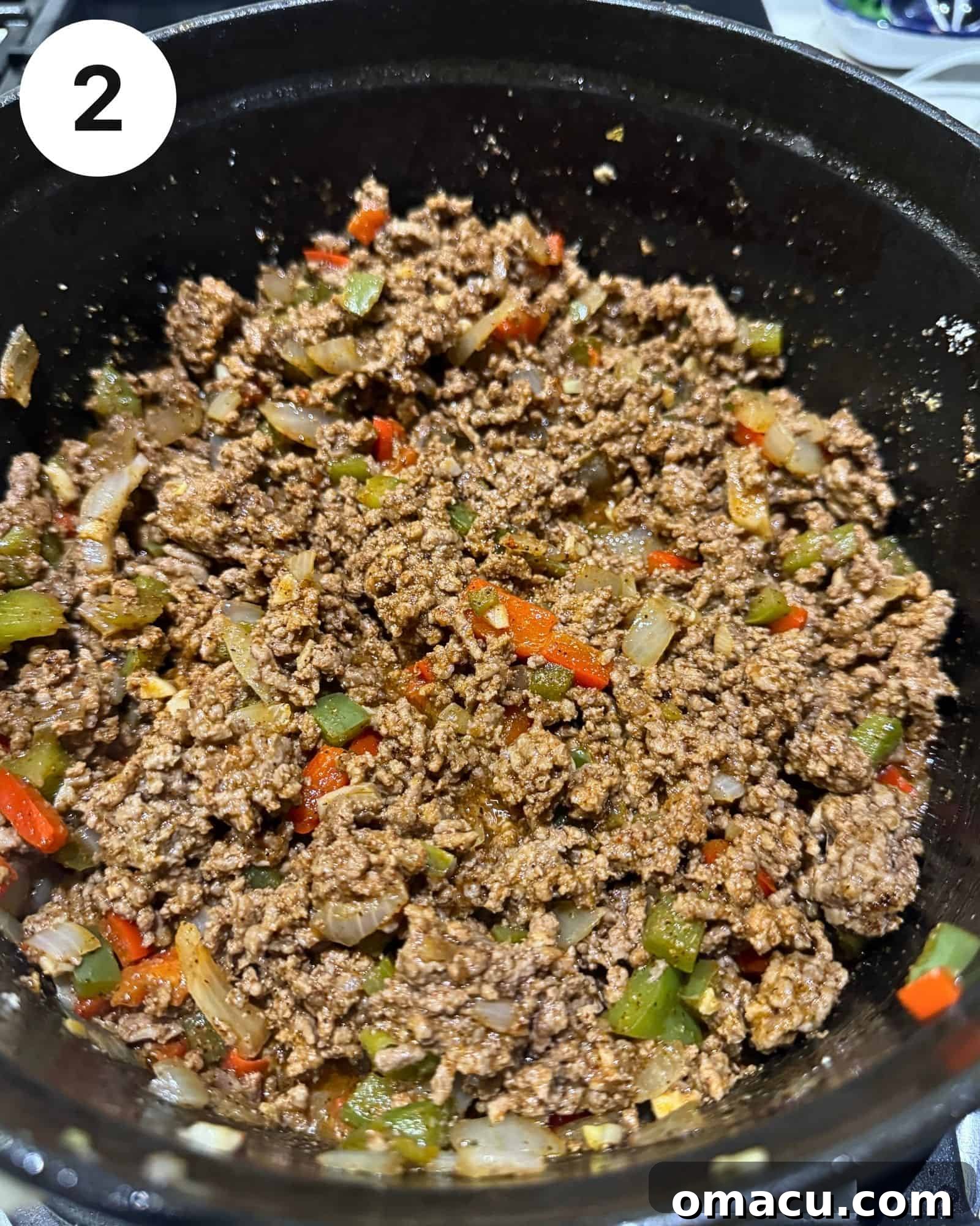 A rich mixture of ground beef, diced bell peppers, onions, garlic, and homemade seasonings browning in a Dutch oven, forming the heart of the chili.