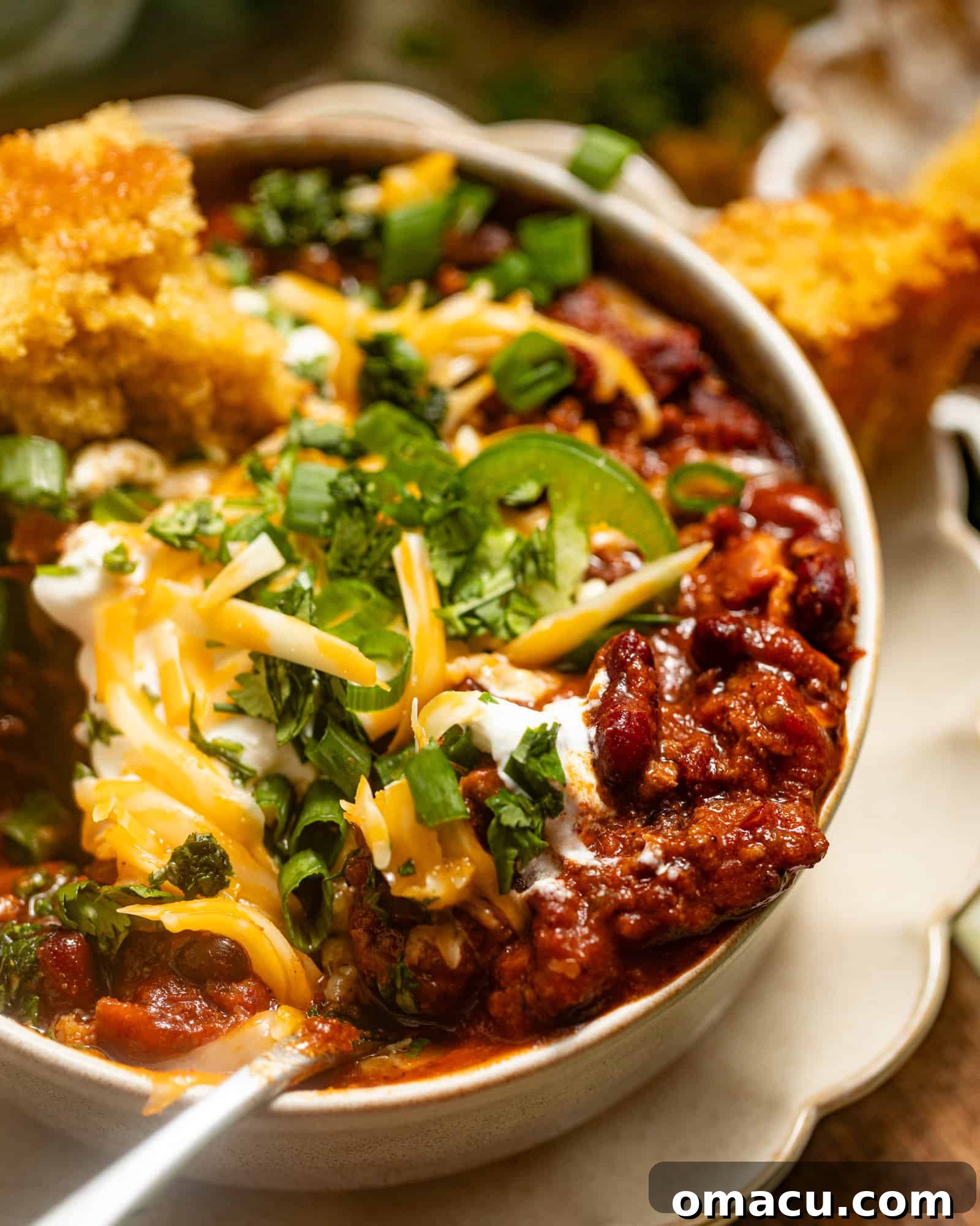 An up-close photo of rich chili on a spoon, generously topped with melted cheese and fresh cilantro, ready to be enjoyed.