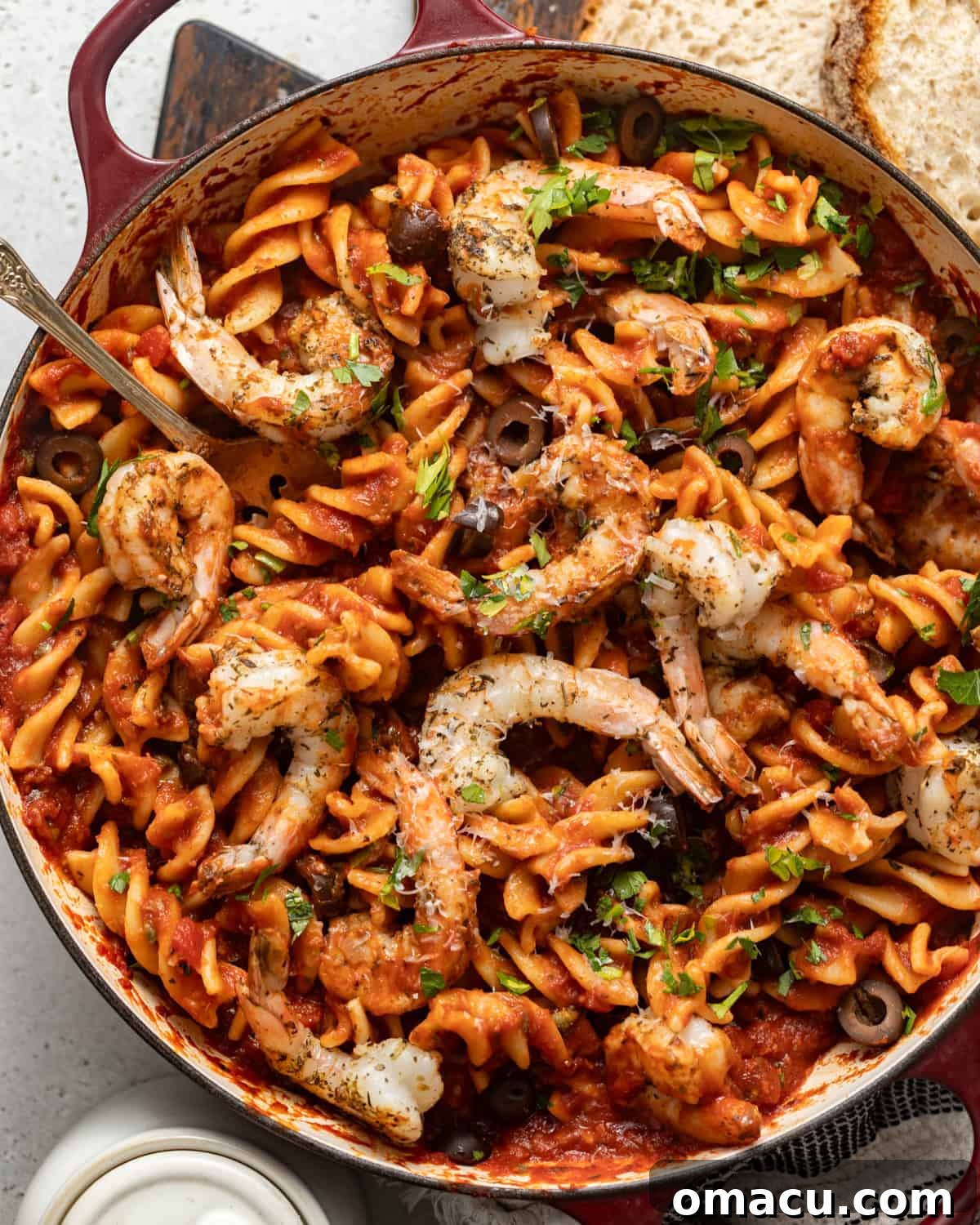 overhead photo of puttanesca with shrimp in a skillet with crusty bread on the side.