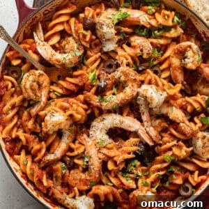 overhead photo of puttanesca with shrimp in a skillet with crusty bread on the side.