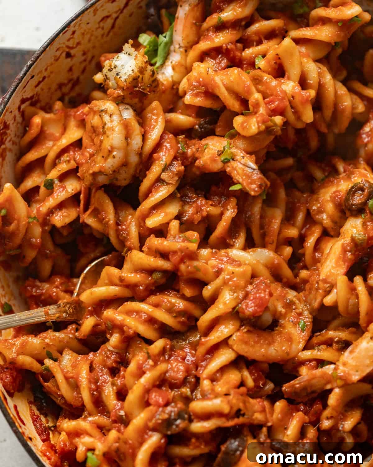 up close photo of cooked pasta puttanesca tossed in sauce.