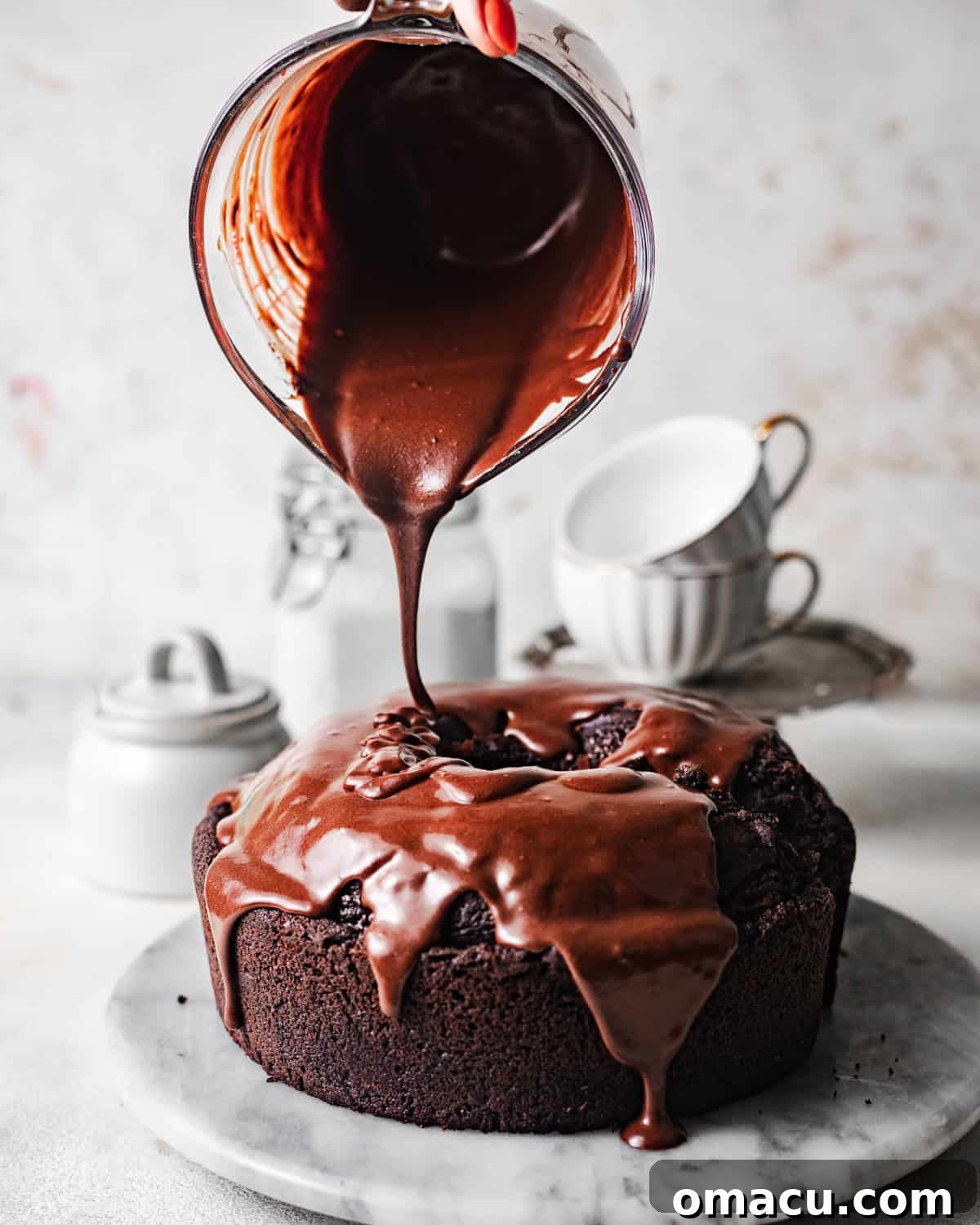 A luscious chocolate ganache is being expertly poured over a freshly baked chocolate ricotta cake, creating a smooth, glossy finish that promises decadent flavor.