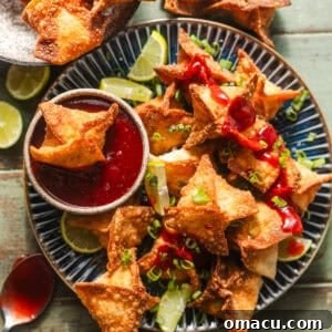 overhead photo of crab rangoons on a plate with homemade sweet and sour sauce in a bowl.