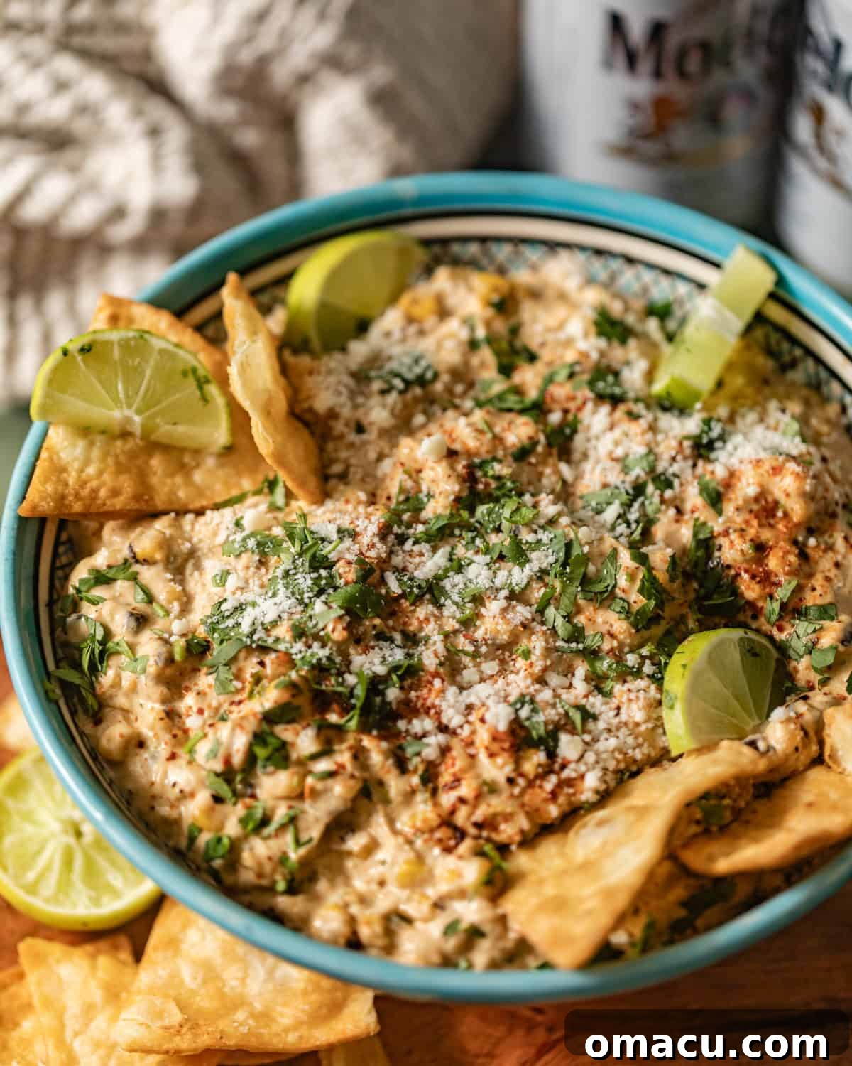 A serving bowl filled with creamy Mexican street corn dip, garnished with fresh cilantro and lime wedges, surrounded by tortilla chips.
