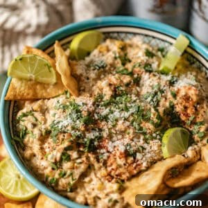 Mexican street corn dip in a bowl with limes and tortilla chips.