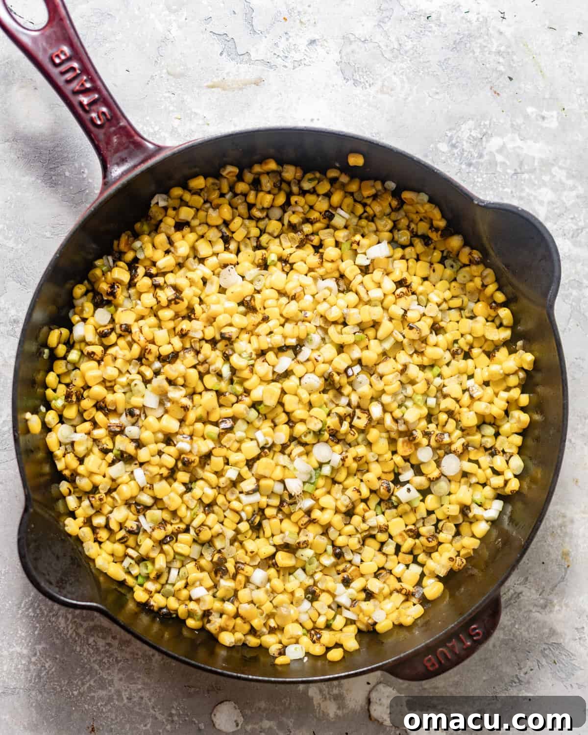 Close-up shot of corn kernels and white scallions sautéing in a cast iron skillet, lightly browned.