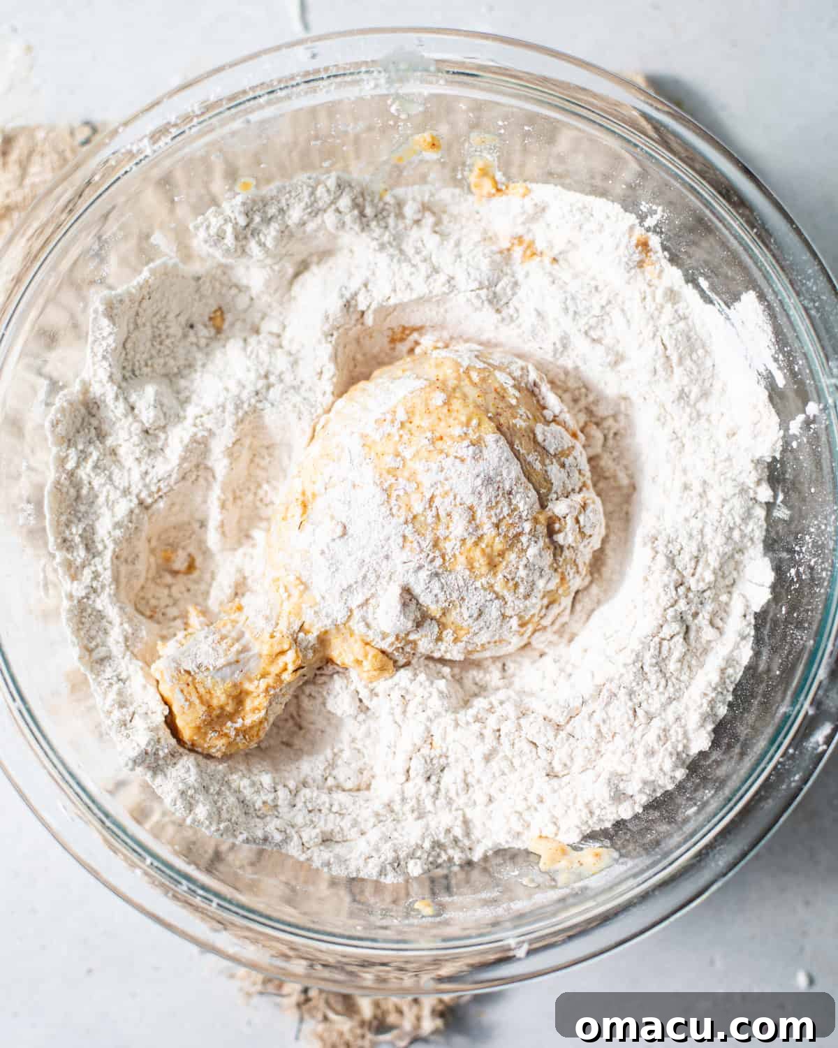 A piece of chicken being carefully coated in a large bowl of seasoned flour, demonstrating the crucial dredging step.