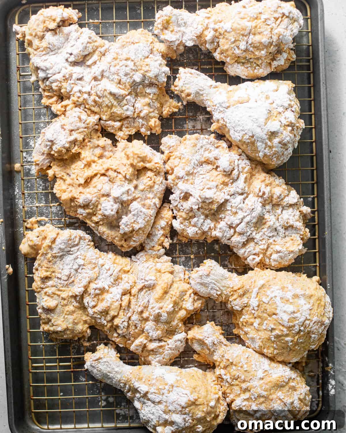 Flour-coated chicken pieces neatly arranged on a wire rack, allowing the coating to set before frying, ensuring maximum crispiness.
