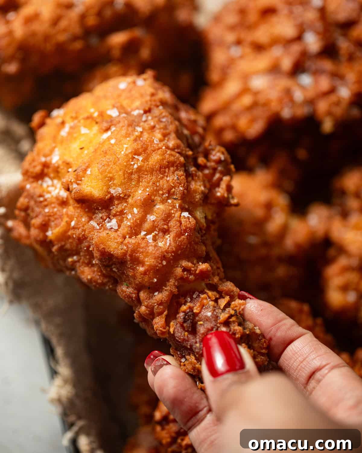 A hand holding a beautifully fried piece of chicken, showcasing its crispy texture.