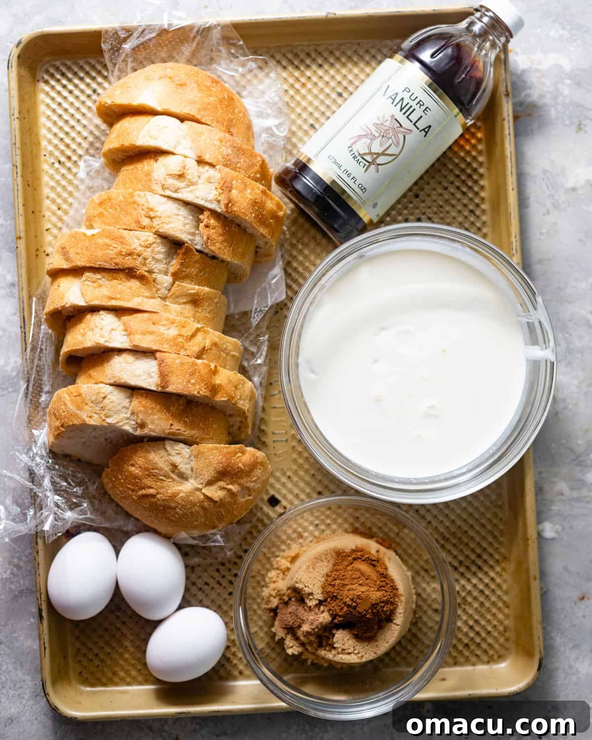 All ingredients for homemade sourdough French toast beautifully laid out on a tray: rustic sourdough bread, farm-fresh eggs, creamy milk, rich heavy cream, aromatic vanilla extract, warm spices like cinnamon and nutmeg, brown sugar, butter, and an optional bottle of bourbon.