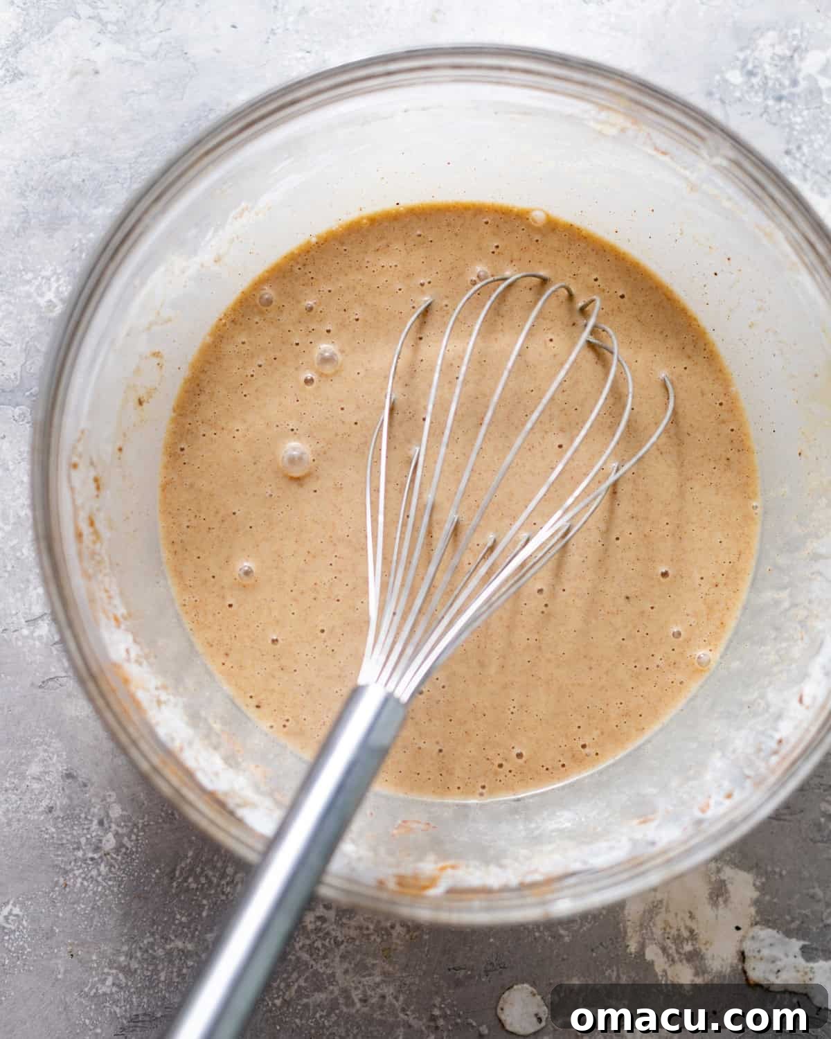 A large mixing bowl containing the French toast custard, showing its creamy texture and flecks of spice, freshly whisked.