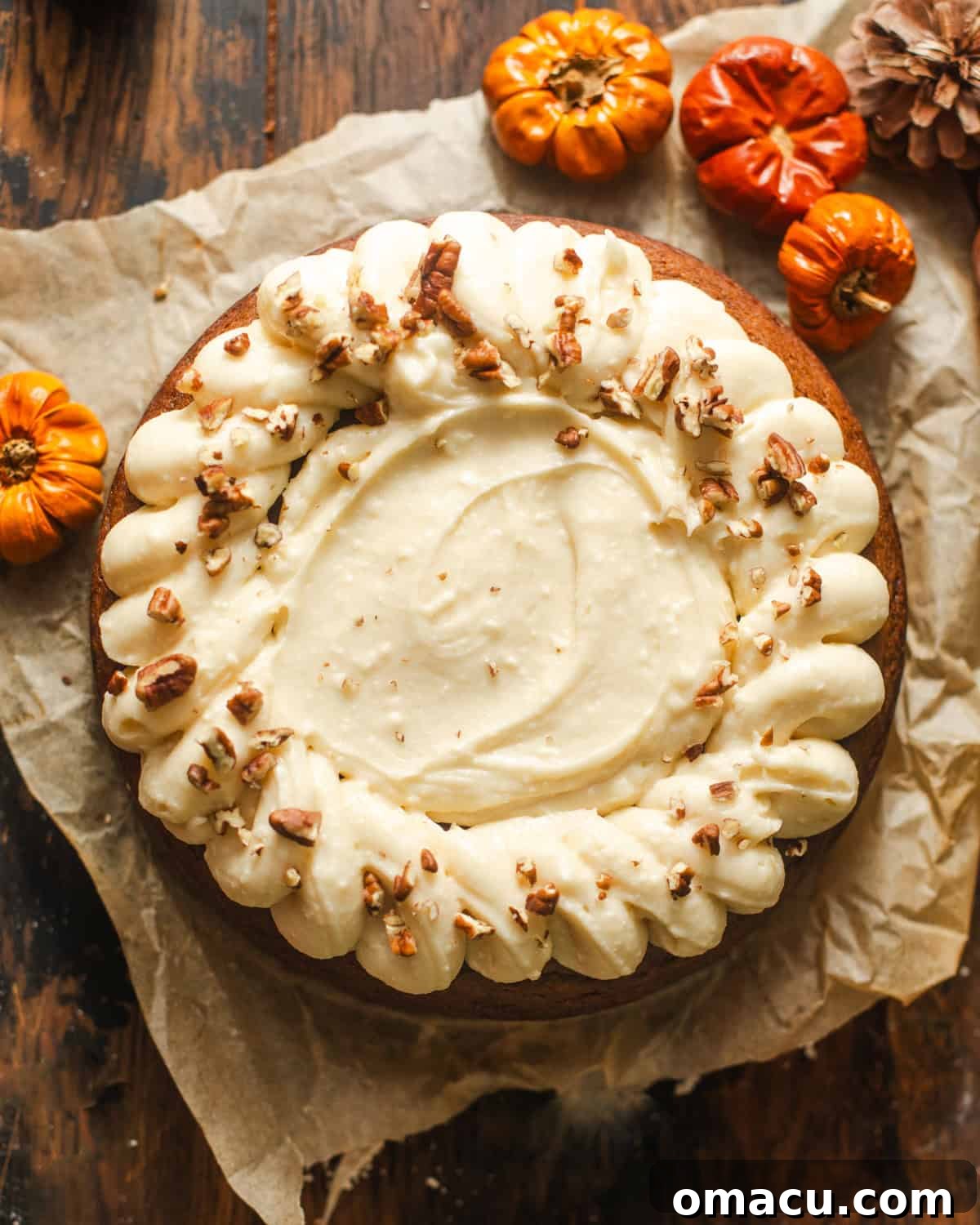 overhead photo of pumpkin olive oil cake on a piece of parchment paper, highlighting its golden hue and generous frosting.