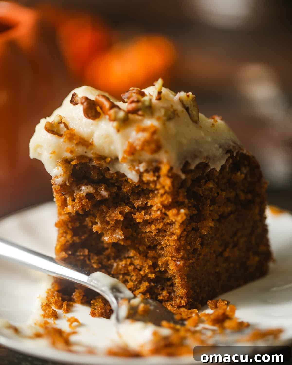 A beautifully presented slice of pumpkin olive oil cake on a white plate, garnished with a fork and hints of fall decor.