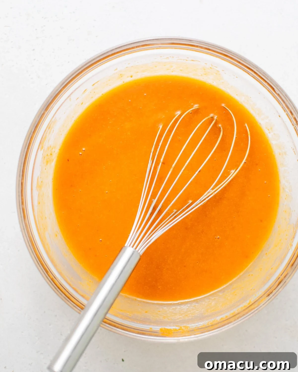 Wet ingredients (pumpkin puree, sugars, olive oil, eggs, vanilla) perfectly whisked together in a large mixing bowl, creating a smooth, orange-hued mixture.