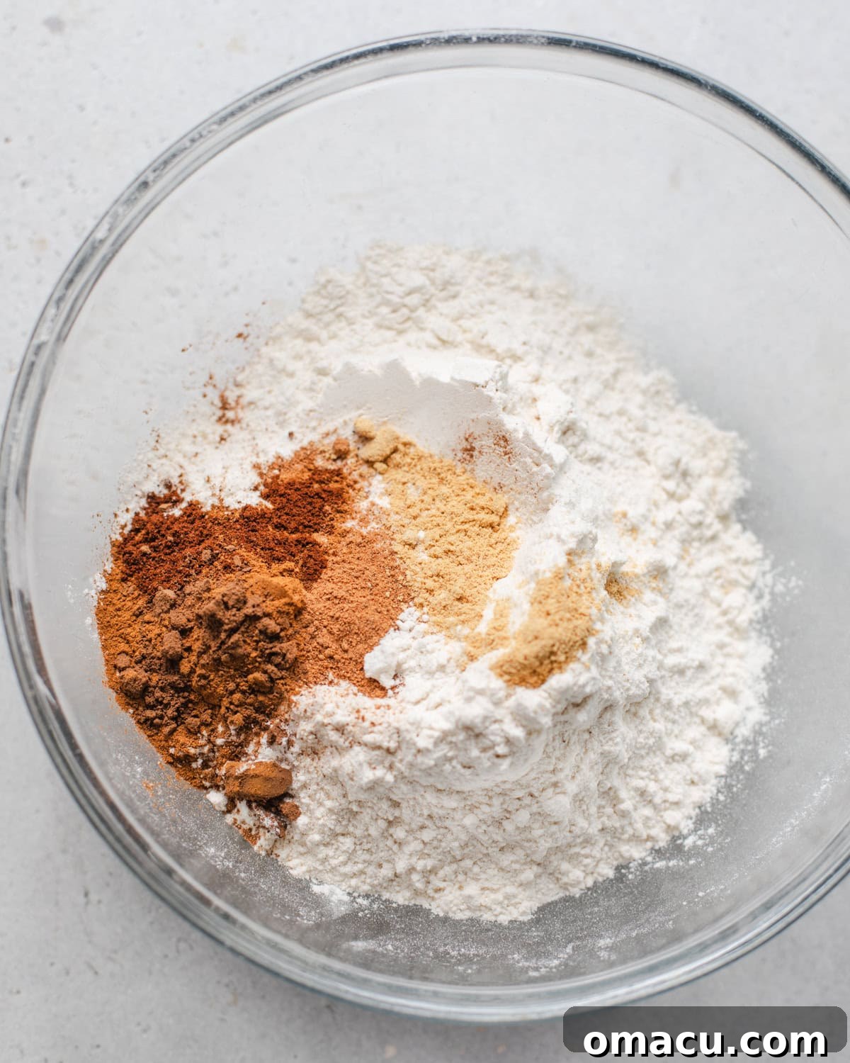 Dry ingredients (flour, baking powder, baking soda, salt, and all the warm spices) neatly whisked together in a separate bowl, ready to be added to the wet mixture.