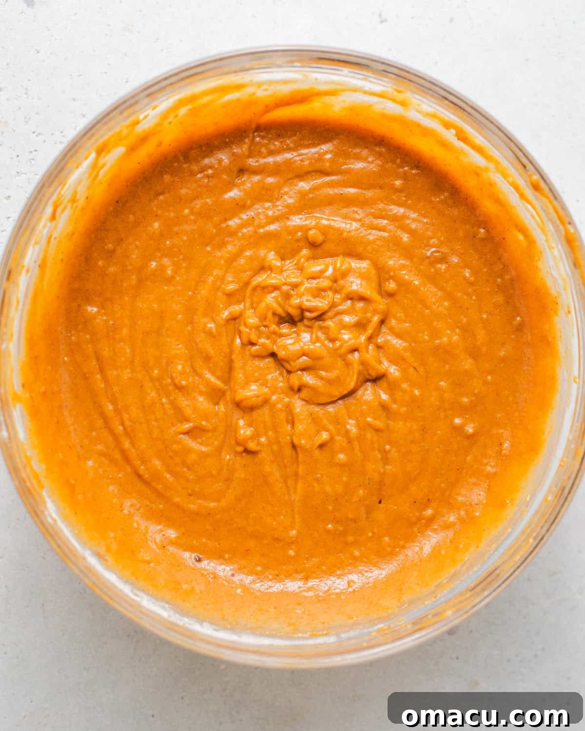 The pumpkin olive oil cake batter, with both wet and dry ingredients mixed together, shown in a mixing bowl with a whisk, illustrating its smooth consistency.