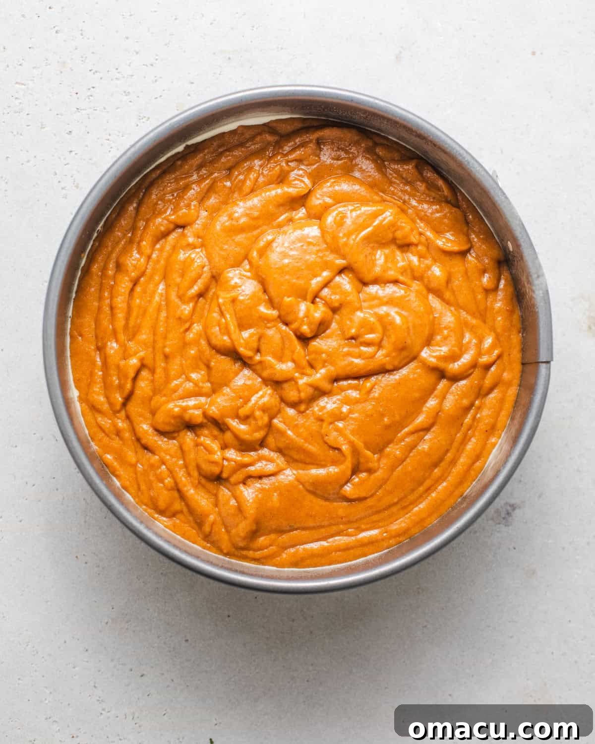 Pumpkin olive oil cake batter poured into a parchment-lined springform pan, ready for baking. The rich orange color of the batter is visible.