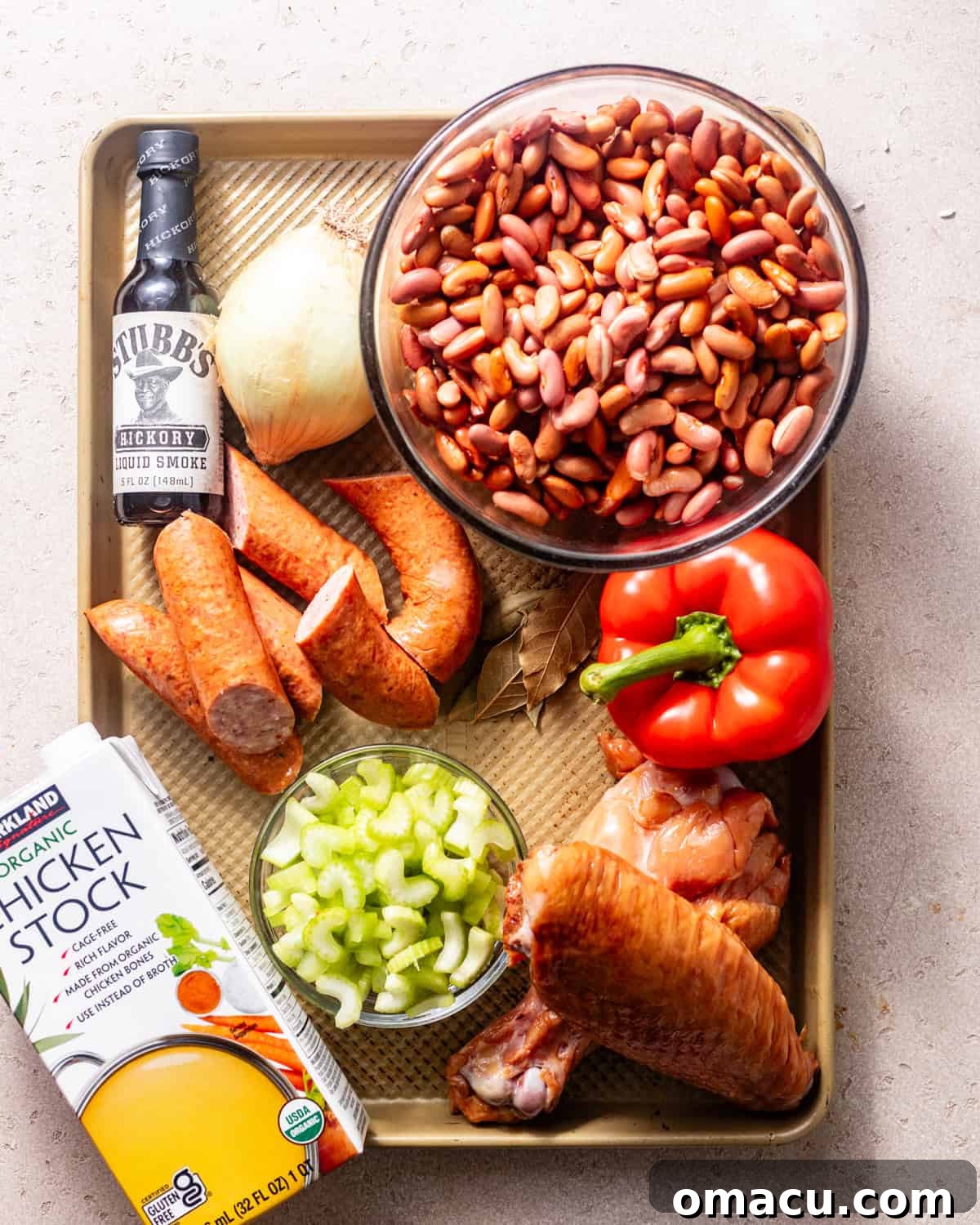 A vibrant display of fresh ingredients for Cajun red beans and rice, including kidney beans, smoked sausage, turkey legs, and the Holy Trinity, arranged on a baking sheet.
