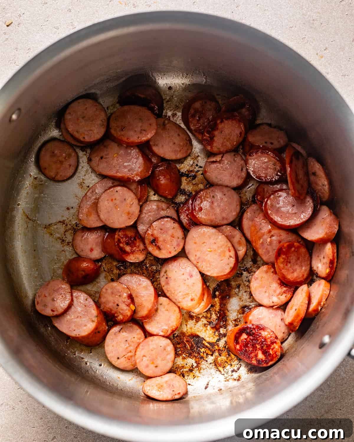 Slices of smoked sausage searing in a large pot or Dutch oven, developing a rich brown crust.