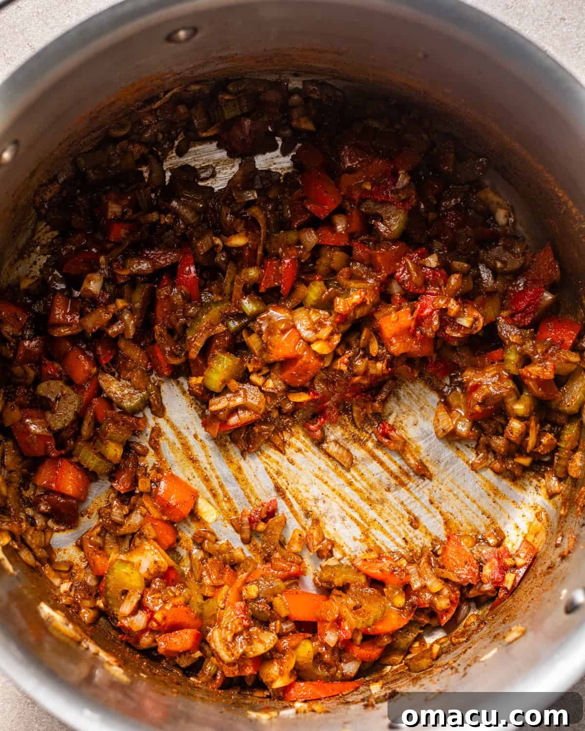 The Holy Trinity of celery, onion, and bell pepper, along with garlic, tomato paste, and seasonings, cooking in a pot.