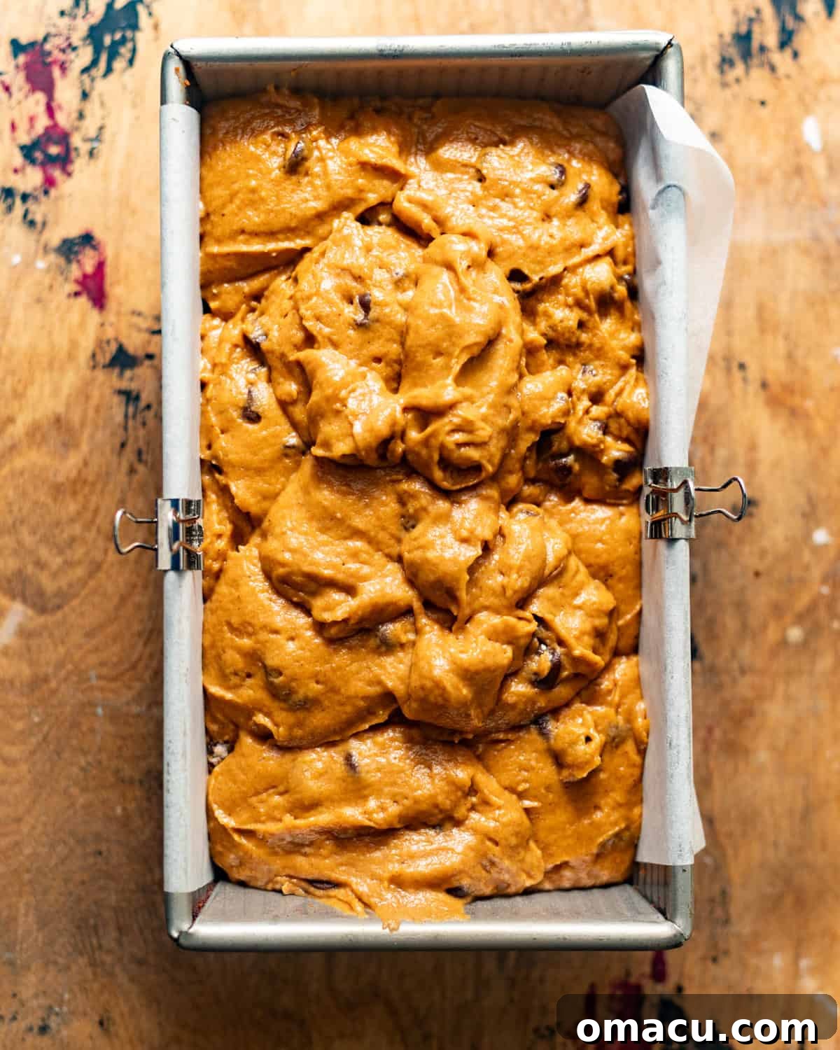 Pumpkin bread batter evenly spread in a parchment-lined loaf pan.