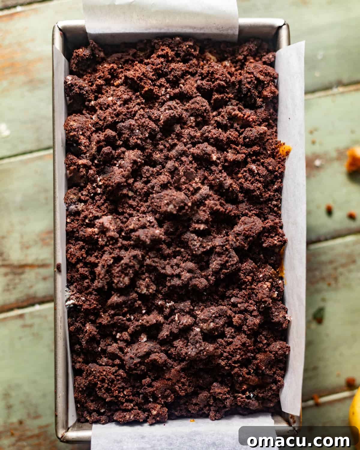 Pumpkin bread batter in a loaf pan with chocolate streusel sprinkled evenly on top.