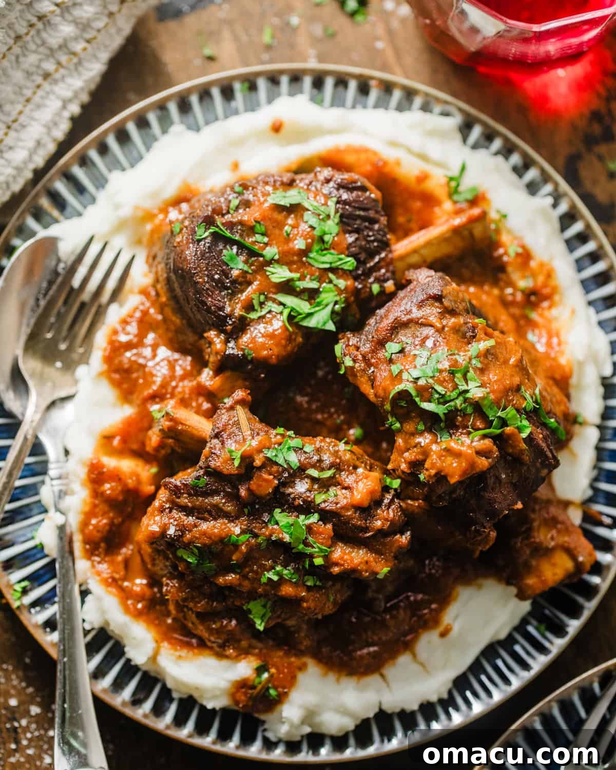 Red wine braised short ribs served on a plate with creamy mashed potatoes and garnished with fresh parsley.