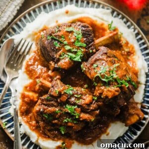 Red wine braised short ribs on a plate with mashed potatoes and garnished with parsley.