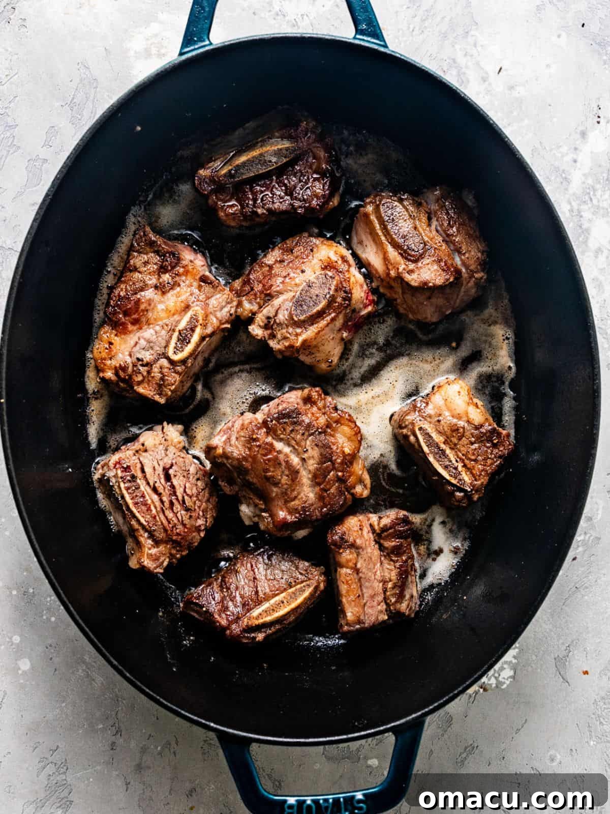 Nicely seared short ribs resting in a large Dutch oven, showing a beautiful golden-brown crust.