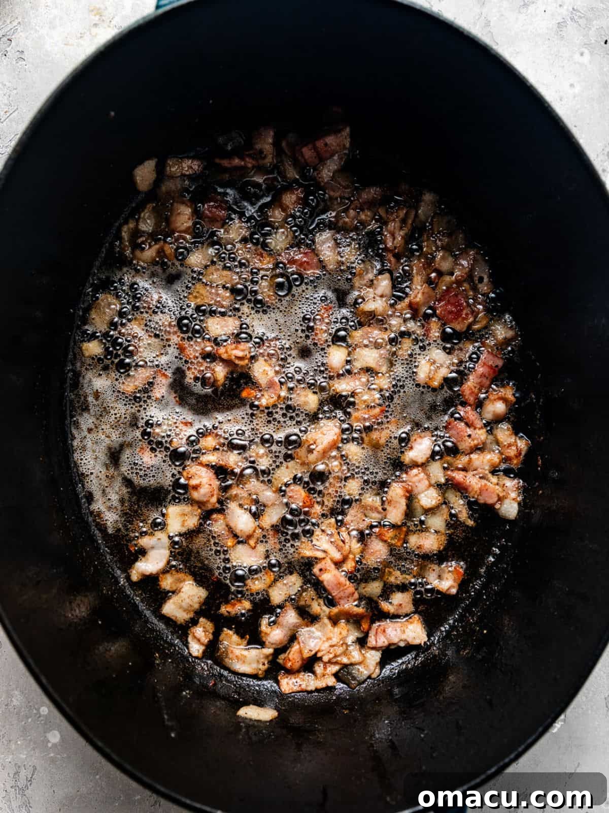 Crispy bacon bits cooking in a large pot, rendering their fat and creating a flavorful base.