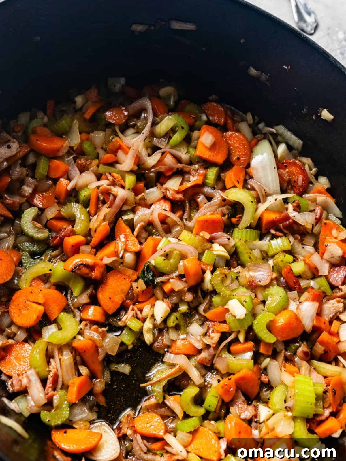 A mix of cooked carrots, celery, onions, shallots, and garlic simmering in a pot, forming the aromatic base for the braise.