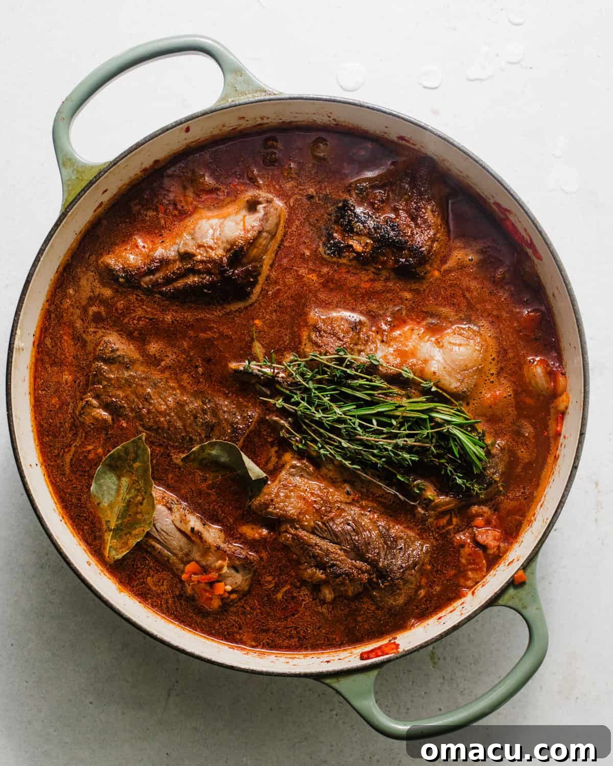 Short ribs nestled back into a large pot, submerged in the braising liquid, with fresh herbs and a parmesan rind infusing flavor.
